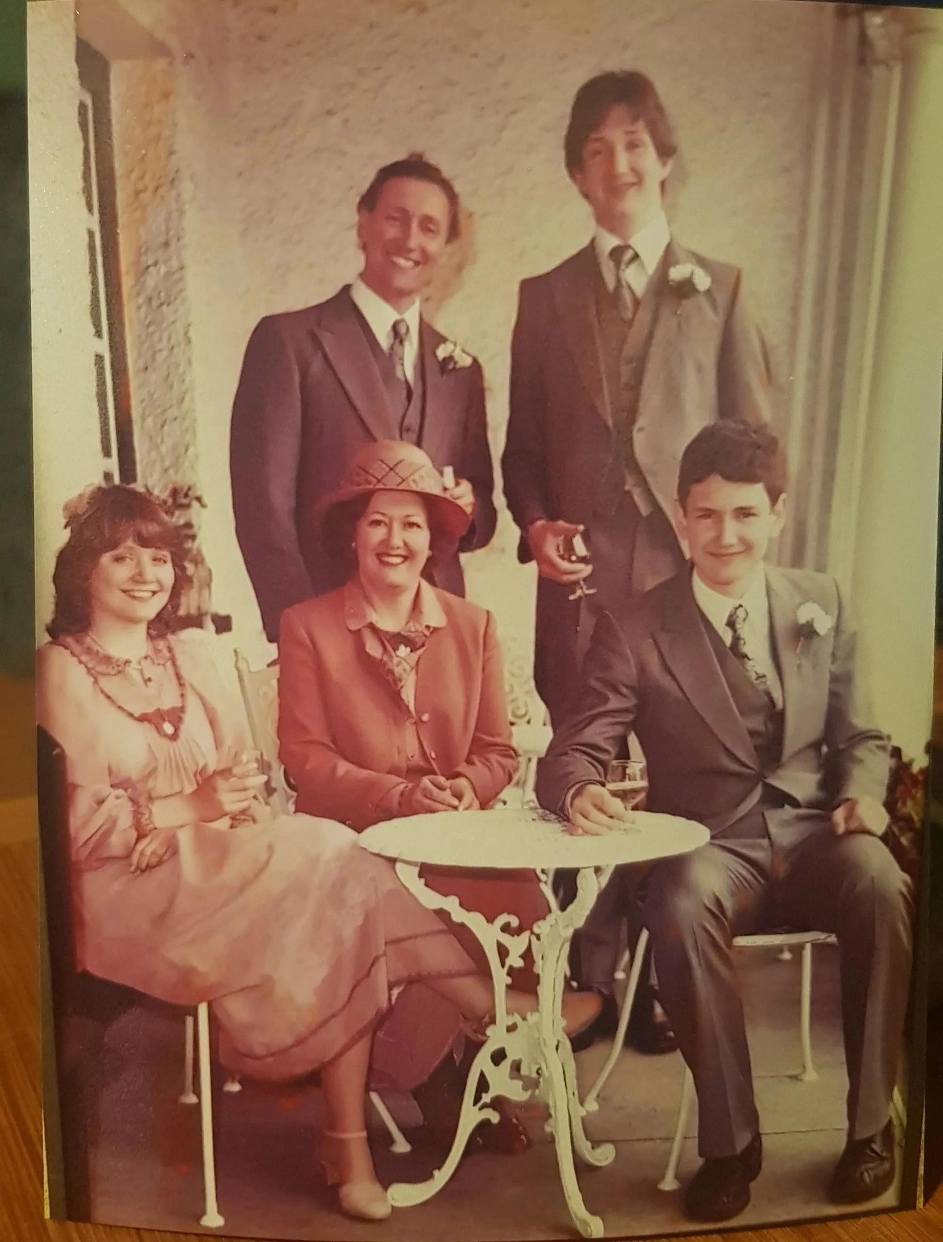 Vintage colour photo of a family of five in formal wear gathered around a small garden table