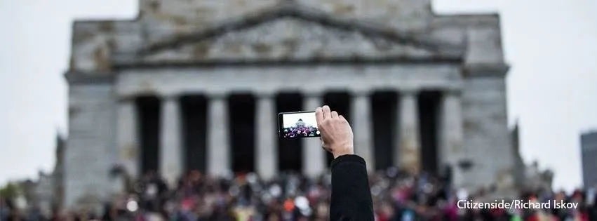 Crowd in front of a classical building, one person filming on a phone