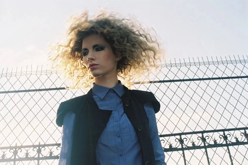 Fashion portrait of a model with curly hair in front of a wire fence