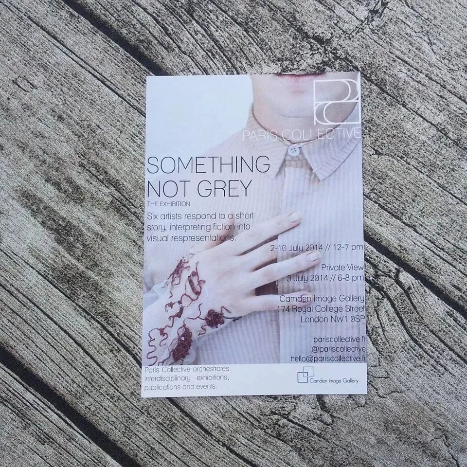 Flyer for the exhibition "Something Not Grey" on a wooden surface