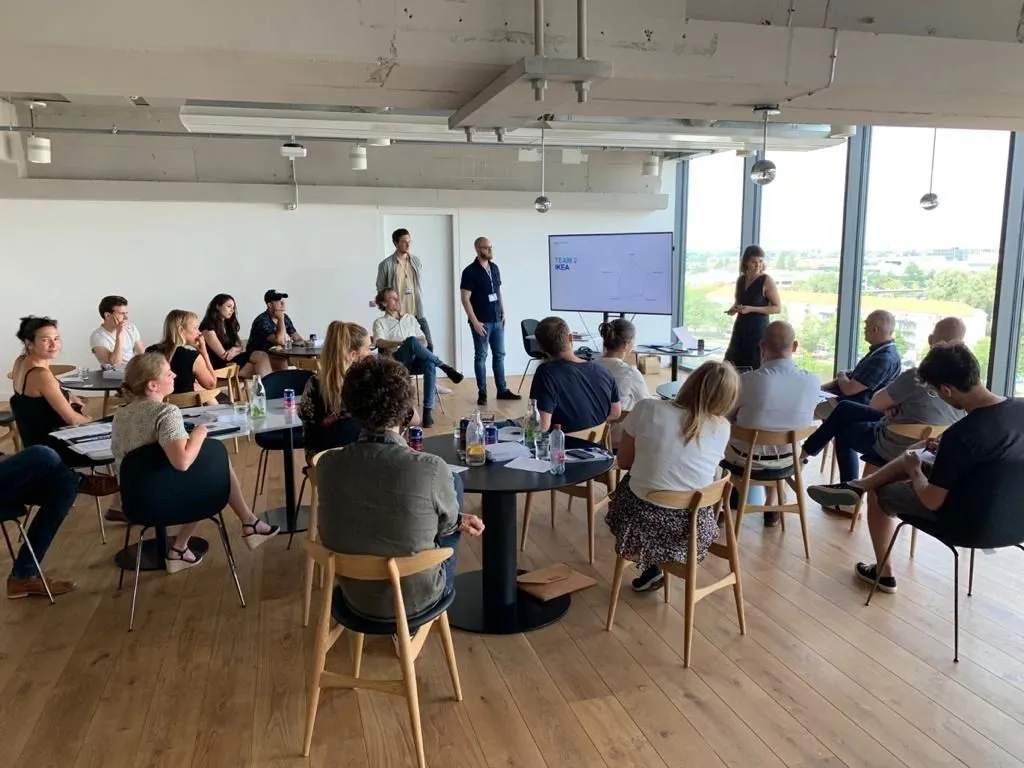 Workshop in a bright office, with a group seated at tables facing a presenter