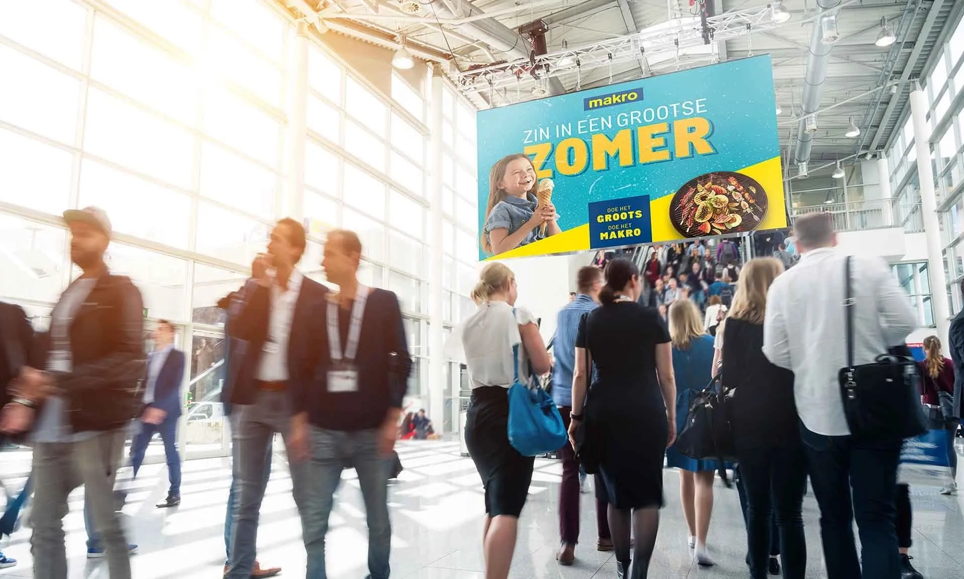 Visitors walking through a trade fair hall under a Makro "Zin in een grootse zomer" banner
