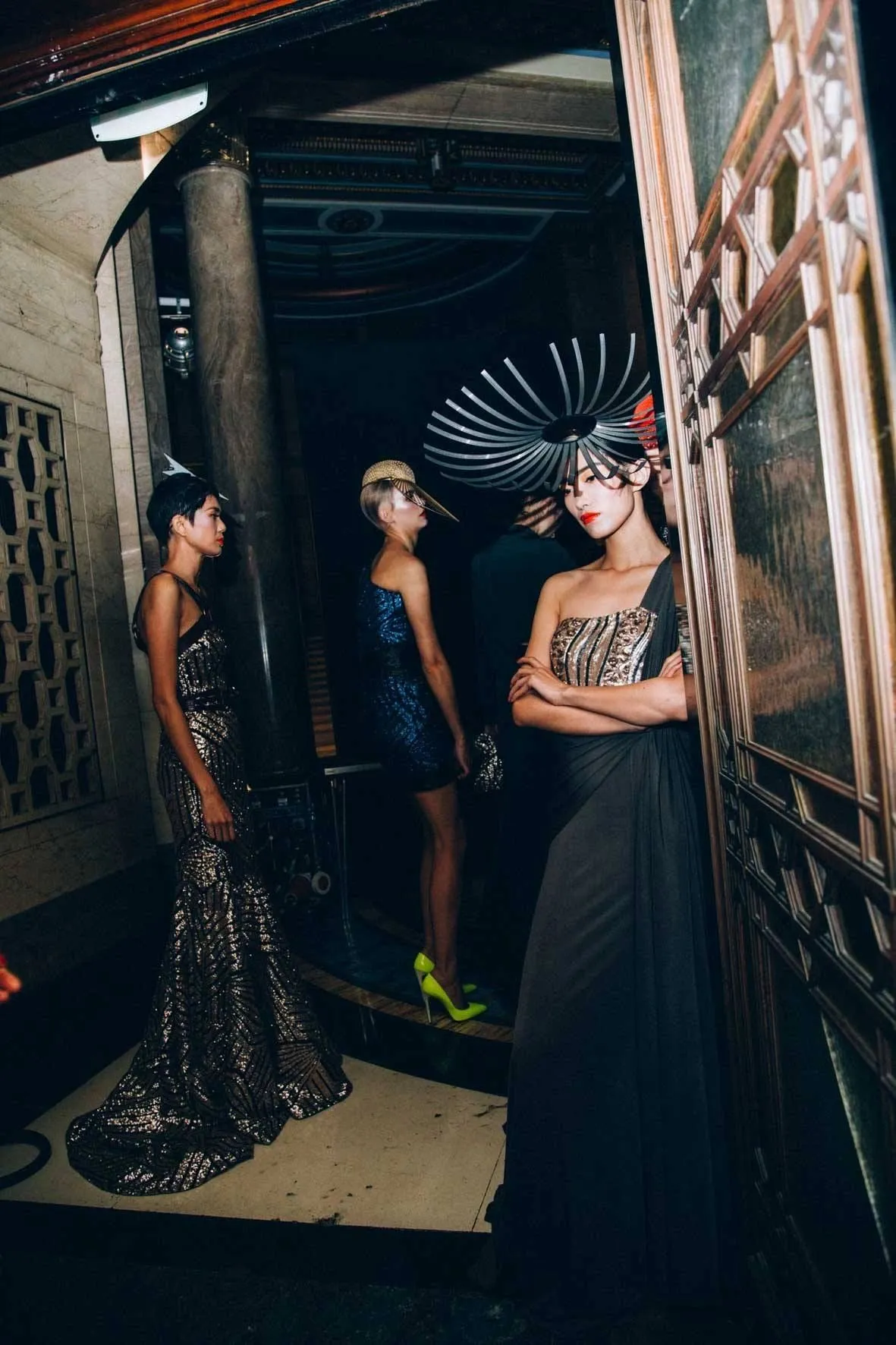 Models in evening wear and headpieces in an ornate doorway